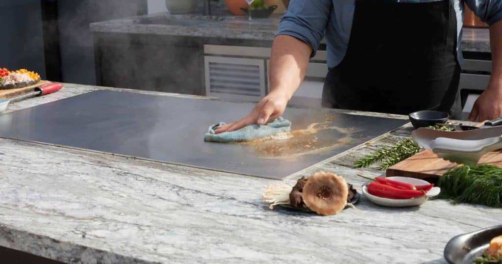 A person wiping down a stainless steel bbq grill to get it clean. 