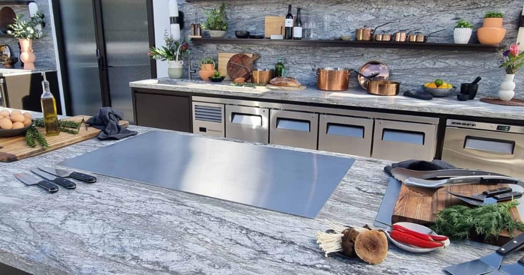 A rooftop kitchen with marbled stone and a large bbq grill plate on the bench. 